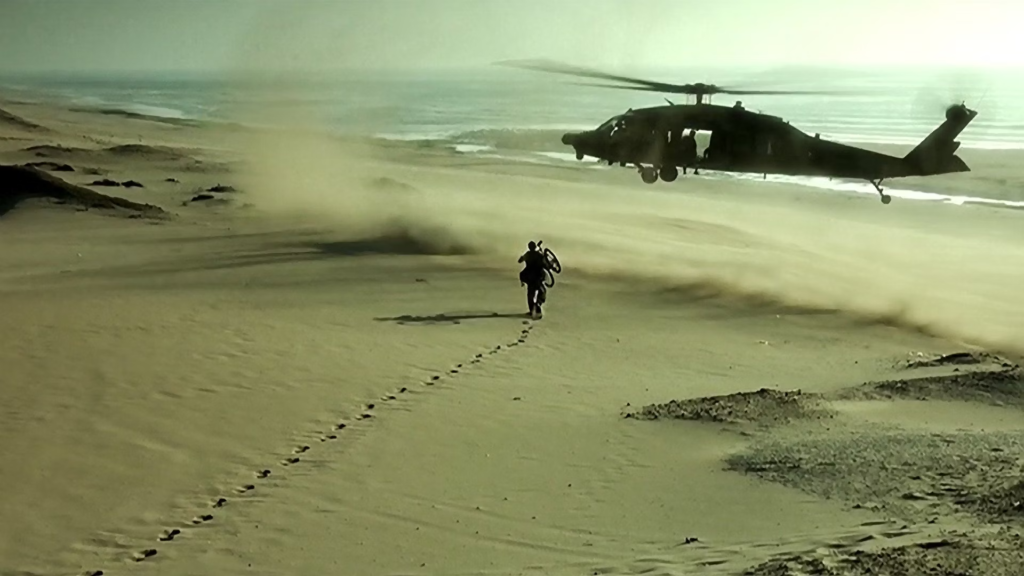 Helicóptero militar resgatando soldado ferido na praia durante uma intensa batalha no filme "Falcão Negro em Perigo"